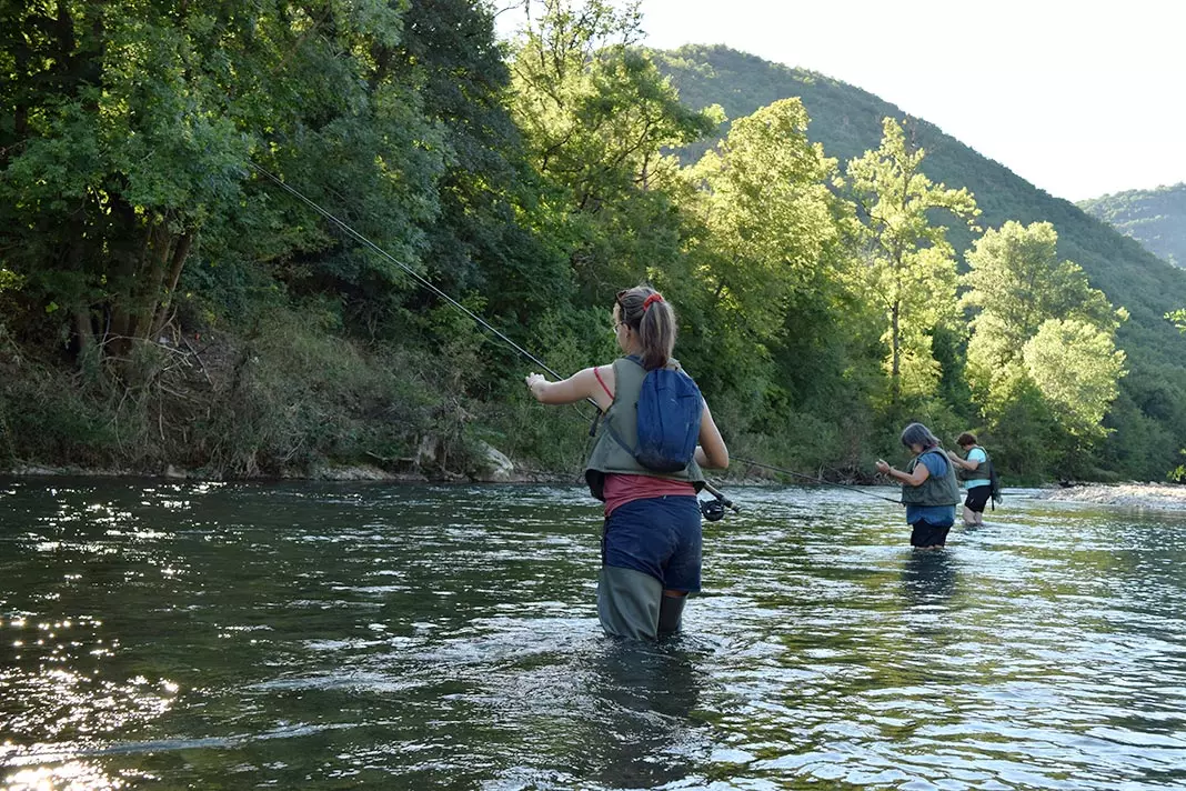 3 femmes pêchent au lancer dans une rivière de l'aveyron ; elles sont concentrées sur leur activité ; des arbres bordent la berge gauche de la rivière