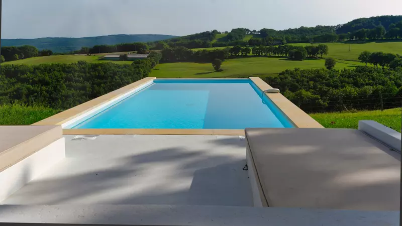 la piscine du gite la cubane près de saint antonin noble val en occitanie, en vue plongeante avec sur le devant une partie de la terrasse blanche, au loin les collines des gorges de l'aveyron ; la piscine est d'un bleu limpide, turquoise