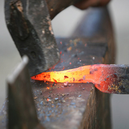 travail de la forge : un bout de métal chauffé au rouge posé sur une enclume avec un marteau de forgeron qui s'abat sur lui