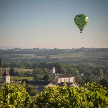 une montgolfière de couleur vert dans un ciel bleu survole un village de la région quercy rouergue gorges de l'aveyron, à proximité de saint-antonin noble val