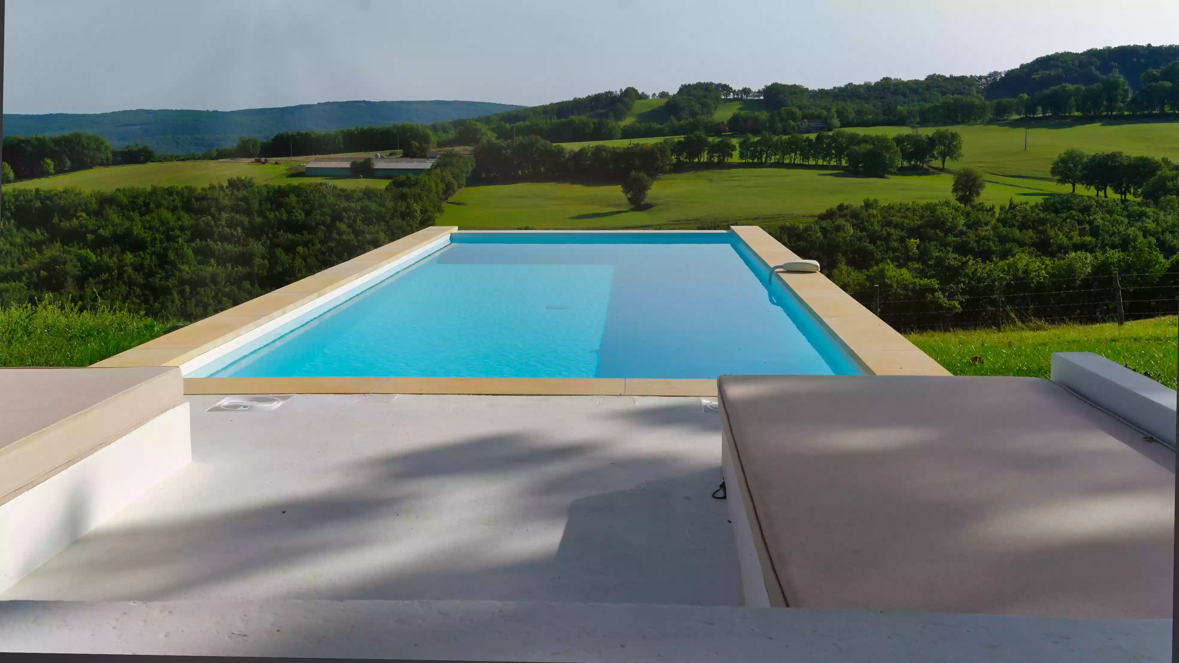 vue en perspective plongeante de la piscine du gîte de la Cubane avec en arrière-plan les collines du Quercy et des gorges de l'Aveyron