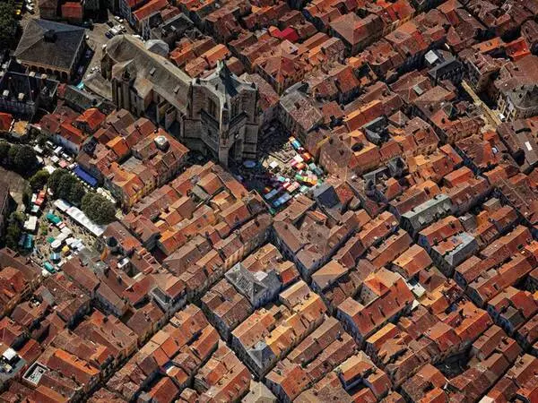 vue aérienne de villefranche de rouergue ; on voit les toitures des maisons, principalement en tuiles, parfois en lauzes ; le plan est en damier et au centre, il y a l'abbatiale notre dame et la grand place