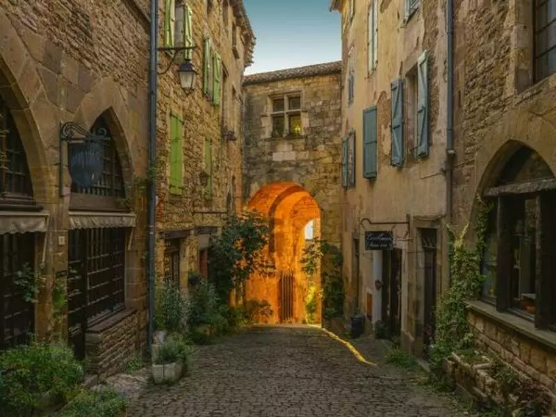 ruelle du village de cordes sur ciel dans le tarn, région occitanie. Au fond de la ruelle, une porte d'enceinte voûtée à travers laquelle passent les rayons du soleil couchant