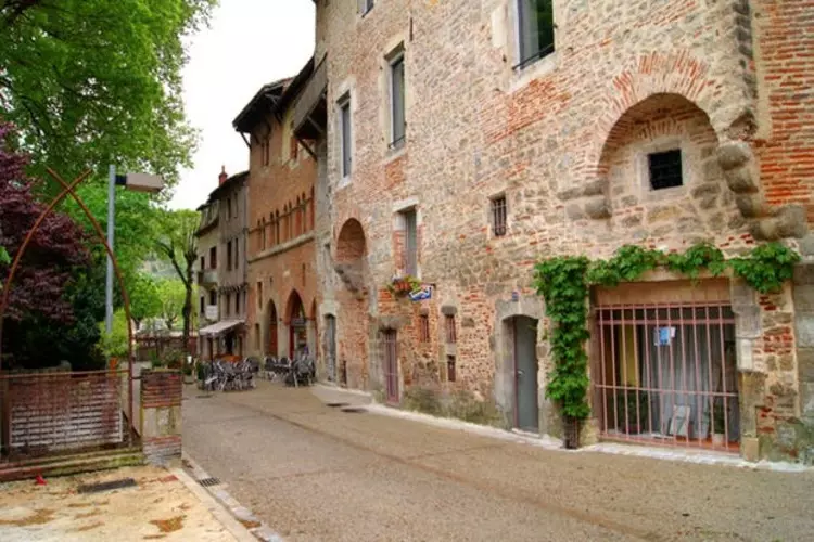 une rue dans le vieux cahors ; maisons en pierre et brique, avec des portes en ogives ; au fond la terrasse d'un café