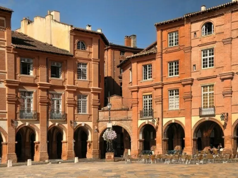 la place Nationale à montauban, en brique rose, avec des maisons à arcades, les terrasses des cafés
