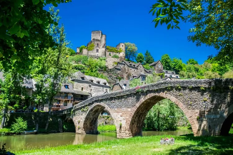 Belcastel en aveyron, occitanie : au premier plan le vieux pont vu de profil avec la rivière aveyron qui coule en dessous ; sur la gauche de la photo, le village ramassé sous le château qui domine