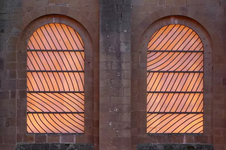 deux vitraux de l'église de conques, couleur orangée en lignes courbes, séparés par un pan de mur en pierre blanche