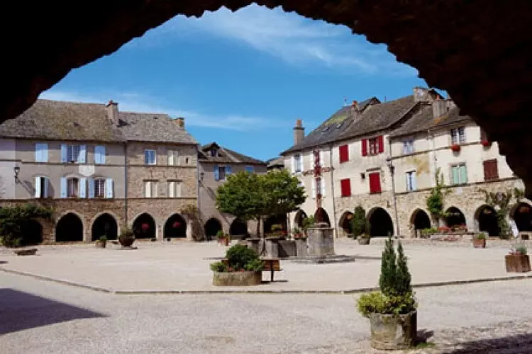 sauveterre de rouergue, bastide de l'aveyron en occitanie ; la grand place vue au travers d'une arcade ; les maisons sont en pierre, avec des arcades en rez de chaussée