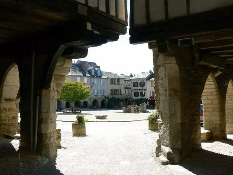 sauveterre de rouergue, village médiéval de l'aveyron dans la région occitanie ; au travers de l'angle de deux maisons, on voit la grand place illuminée de soleil, avec les maisons à arcades