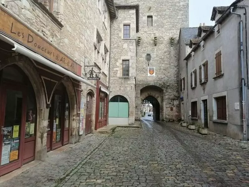 villeneuve d'aveyron en occitanie ; on voit une rue de cette cité médiévale, avec en fond la porte d'enceinte avec un arc brisé et la herse relevée